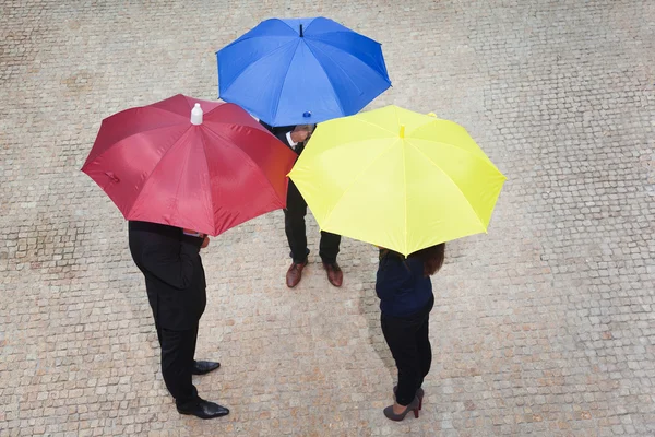 Geschäftsleute unter bunten Regenschirmen versteckt — Stockfoto