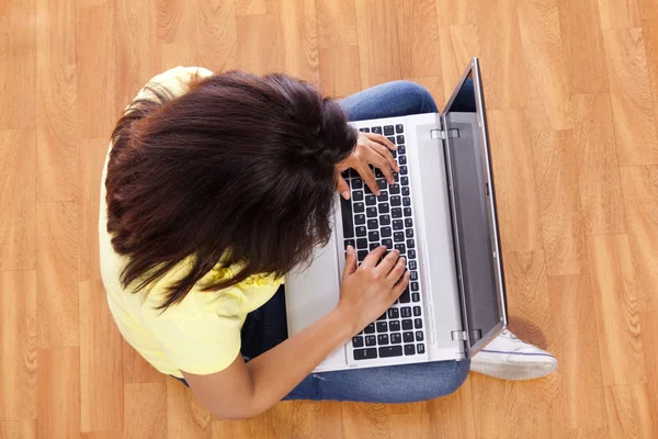 Женщина сидит на полу и работает с ноутбуком дома — стоковое фото