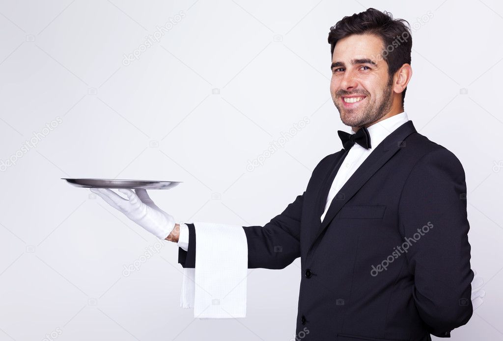 Handsome waiter holding an empty silver tray over gray backgroun