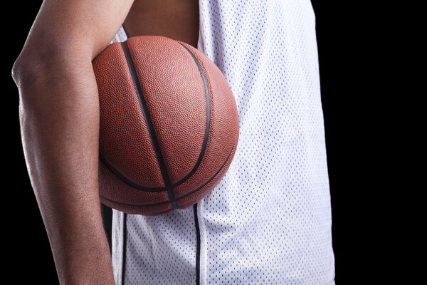 Basketball player holding a ball against dark background