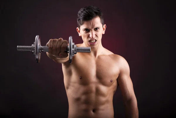 Imagem de um jovem musculoso levantando pesos no backgroun preto — Fotografia de Stock