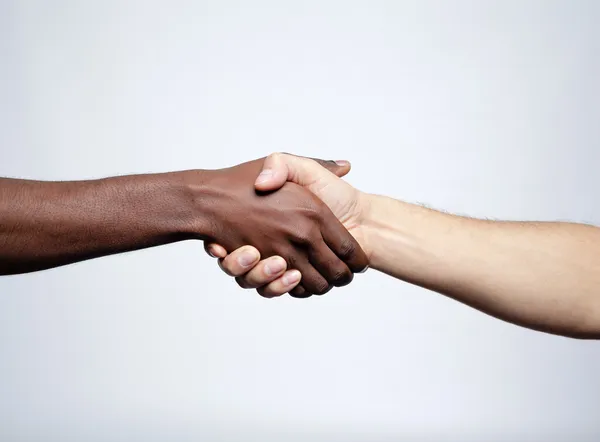 Рукостискання між африканцем і кавказьким чоловіком над сірим бекграу — стокове фото
