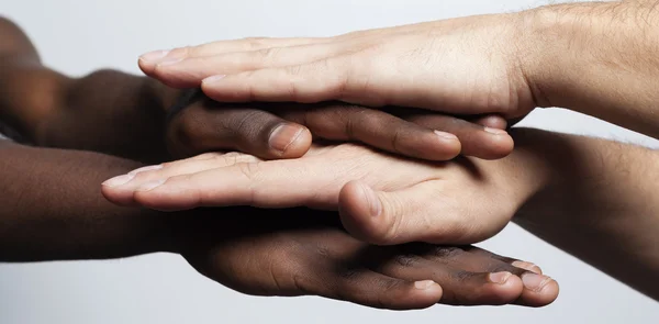 Mãos multirraciais juntos formando uma pilha sobre fundo cinza — Fotografia de Stock