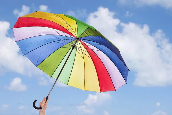 Rainbow umbrella in woman hands against cloudy sky — Stock Photo, Image