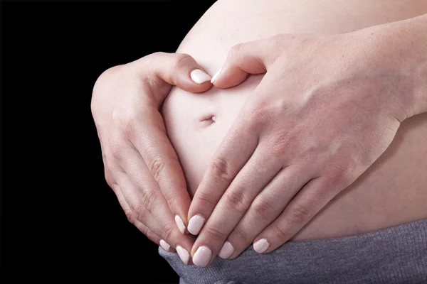 Schwangere Frau hält ihre Hände in Herzform auf ihrem Bauch — Stockfoto