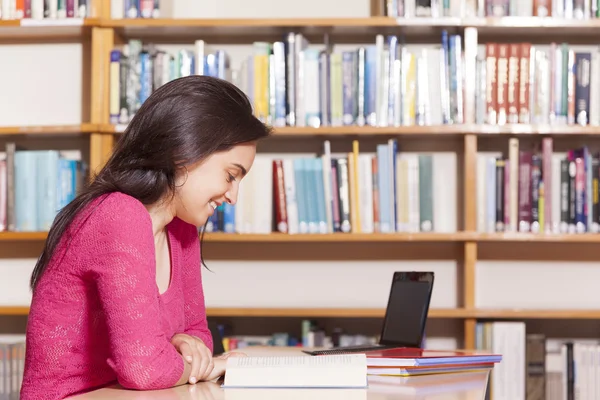 Smiling female student studying in a library — Stock Photo, Image