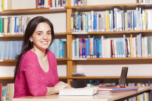 Estudante do sexo feminino sorrindo estudando em uma biblioteca — Fotografia de Stock