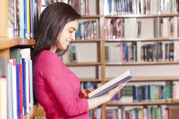 Portrait of a smiling young student reading a book in a library — Stock Photo, Image