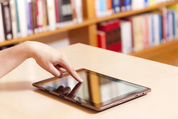 Mão digitando no tablet pc na biblioteca — Fotografia de Stock