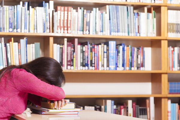 Tired student girl sleeping on the table at the library