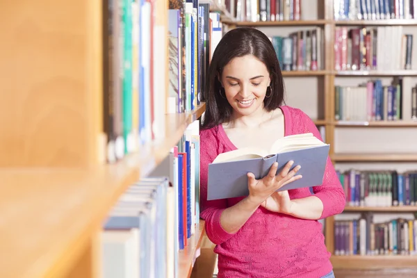 Retrato de um jovem estudante sorrindo lendo um livro em uma biblioteca — Fotografia de Stock
