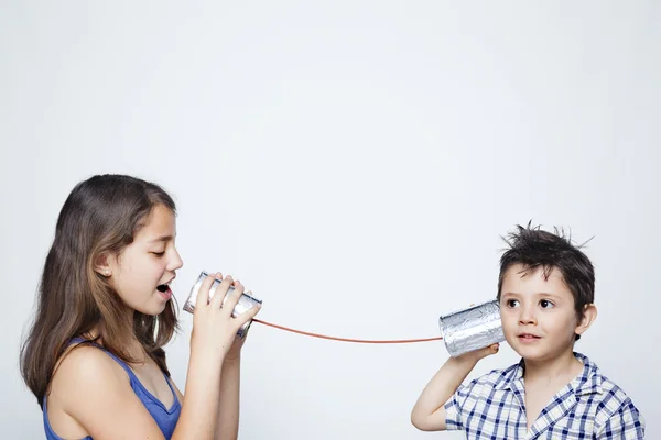 Kinderen met behulp van een blikje als telefoon tegen een grijze achtergrond — Stockfoto
