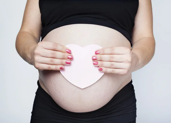 Těhotná žena drží srdce na břiše — Stock fotografie
