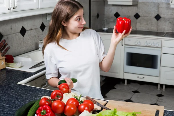 Mujer joven en la cocina mirando pimiento rojo — Foto de Stock