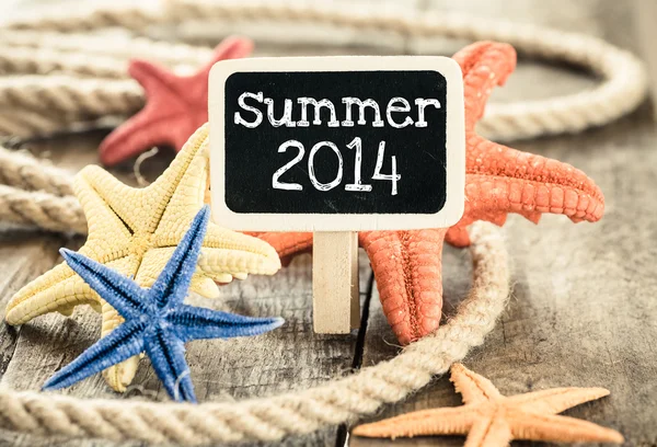 Cáscaras de mar y cuerda sobre fondo de madera con pizarra pequeña y texto verano 2014 —  Fotos de Stock