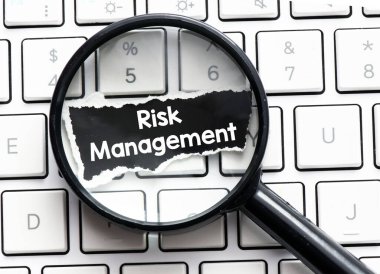 Risk Yönetimi konsepti. Bir klavyeye yerleştirilmiş bir büyüteç ve üzerinde risk yönetimi yazan siyah bir kağıt parçası..