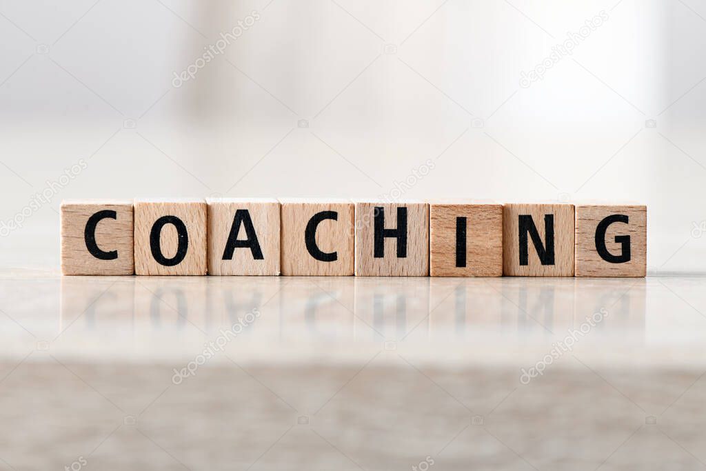 Word COACHING arranged from wooden letters on light background. Concept for business.