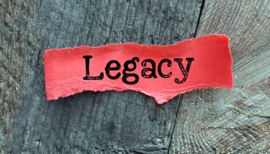 LEGACY word on small red sheet of paper and wooden background. clipart