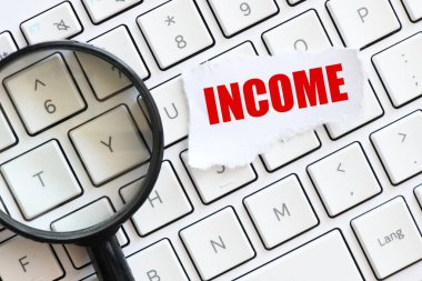 INCome kelimesi, büyüteçin yanına bir bilgisayar klavyesine yerleştirilmiş küçük bir kağıt üzerinde. İş kavramı