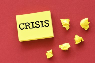 Küçük sarı bir kağıt parçası ve kırmızı bir arkaplan üzerinde CRISIS kelimesi.