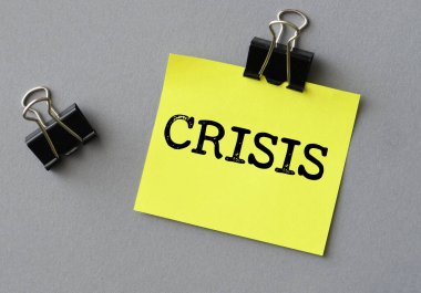 Küçük sarı bir kağıt parçası ve gri bir arkaplan üzerinde CRISIS kelimesi.