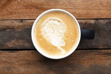 Tahta bir masanın üzerinde kahve olan beyaz bir fincan..