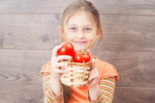 Beautiful little girl holding wicker basket with red tomatoes — Stock Photo, Image