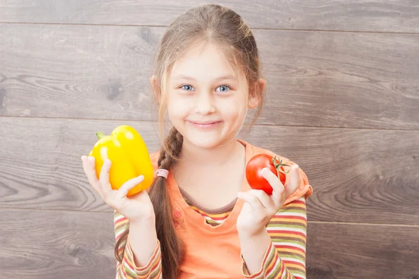 Smiling little girl holding fresh vegetables on a wooden backgro — Stock Photo, Image