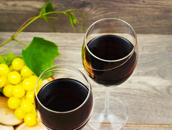 Dois copos de vinho tinto e uvas em um fundo de madeira — Fotografia de Stock