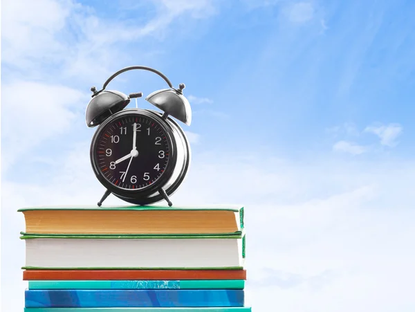 Libros y un reloj despertador sobre un fondo de cielo azul — Foto de Stock