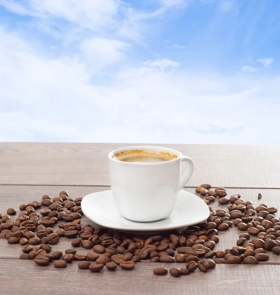Šálek kávy a kávových zrn na pozadí modré oblohy — Stock fotografie