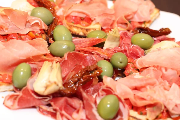 Primo piano dei bruschetti con prosciutto e olive su un piatto — Foto Stock