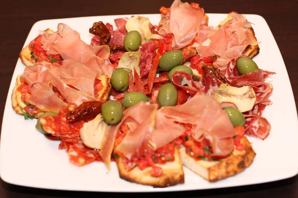 Placa de bruschetti con jamón y aceitunas verdes —  Fotos de Stock