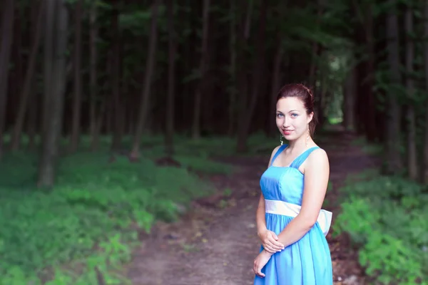 Leende flicka står på en gångstig i mörka skogen — Stockfoto