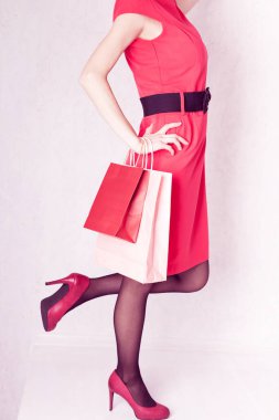 Kırmızı elbiseli ve topuklu ayakkabılı bir kız elinde paketler tutuyor.