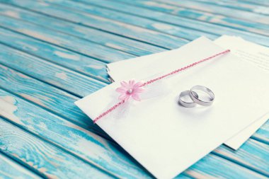 Pembe çiçekle süslenmiş zarf ve mavi arka planda iki alyans.