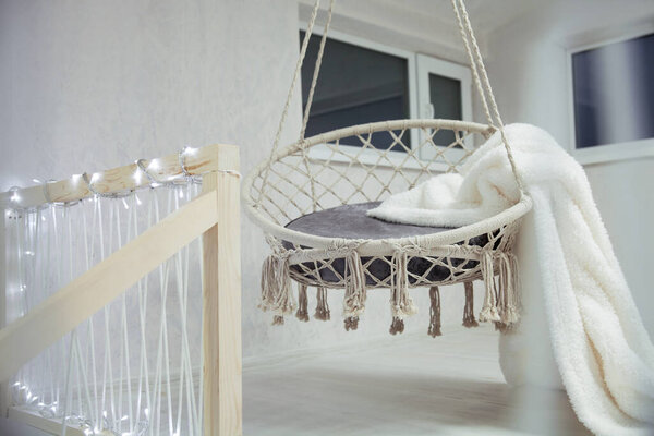 Жду Рождества. Висячий стул с белым мехом в клетку на фоне комнаты, украшенной гирляндами