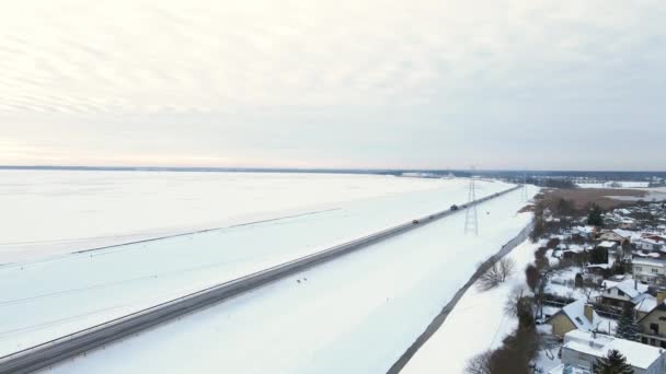 Линии электропередач с башнями рядом с дорогой с движением и деревней зимой — стоковое видео