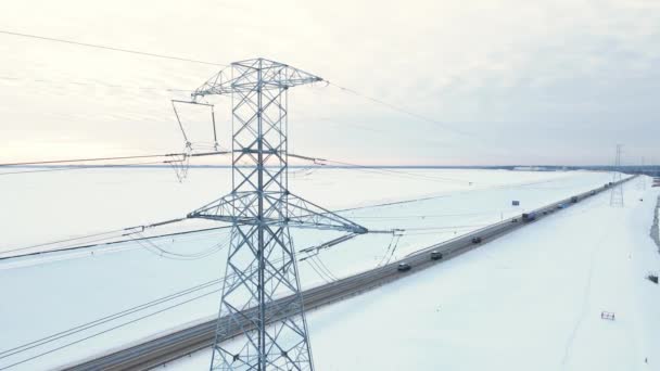 Εναέρια pan up: Ηλεκτρικές γραμμές με πύργους κοντά στο δρόμο με κίνηση το χειμώνα — Αρχείο Βίντεο