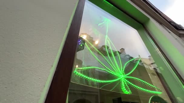 Großes grünes Neon-Cannabis-Blatt an Schaufenster eines Cafés in der Stadtstraße — Stockvideo