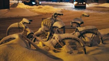 Bisikletler kış gecesi şehir merkezindeki bisiklet parkında karla kaplıydı.