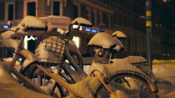 Два велосипеди, вкриті снігом, припарковані в центрі міста з трафіком і людьми на задньому плані — стокове відео