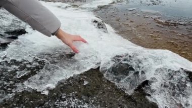 Baharda nehirde eriyen buz kütlelerine ve buz saçaklarına dokunan kadın eli