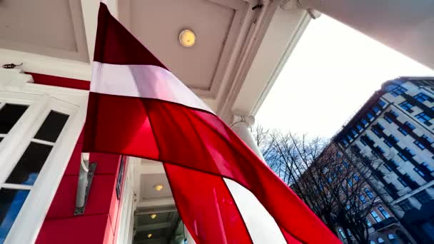 ЩАСТЯ латвійського прапора висить на вітрі, встановленому у старому міському будинку. — стокове відео