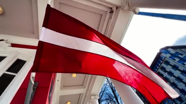 LARGE Латвійський прапор пурхає на вітрі, встановленому в старому міському будинку — стокове відео
