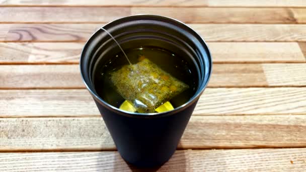 Still shot of thermal cup with green tea bag inside on wooden table — Stock Video