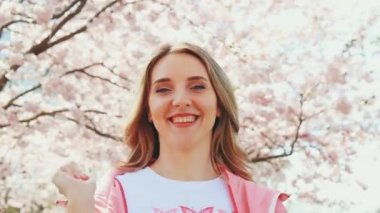 Pembe ve beyaz giysili mutlu bir kadın çiçek açan sakura ya da kiraz ağaçlarına hava öpücüğü verir.