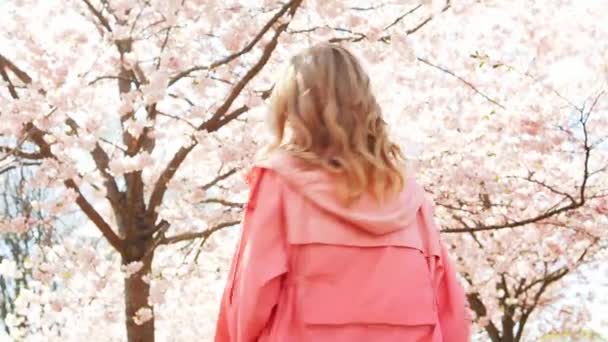 Happy woman smiling and looking at you under blossoming sakura or cherry tree — 비디오