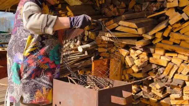 Oudere vrouwelijke boer zet gehakt brandhout van een grote houten muur in een draagkist in een Oekraïens dorp — Stockvideo