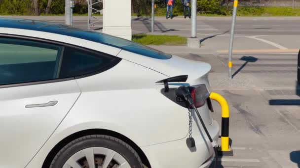 近代的な白い電気自動車はショッピングモールの近くのE車充電ステーションで充電されます。 — ストック動画